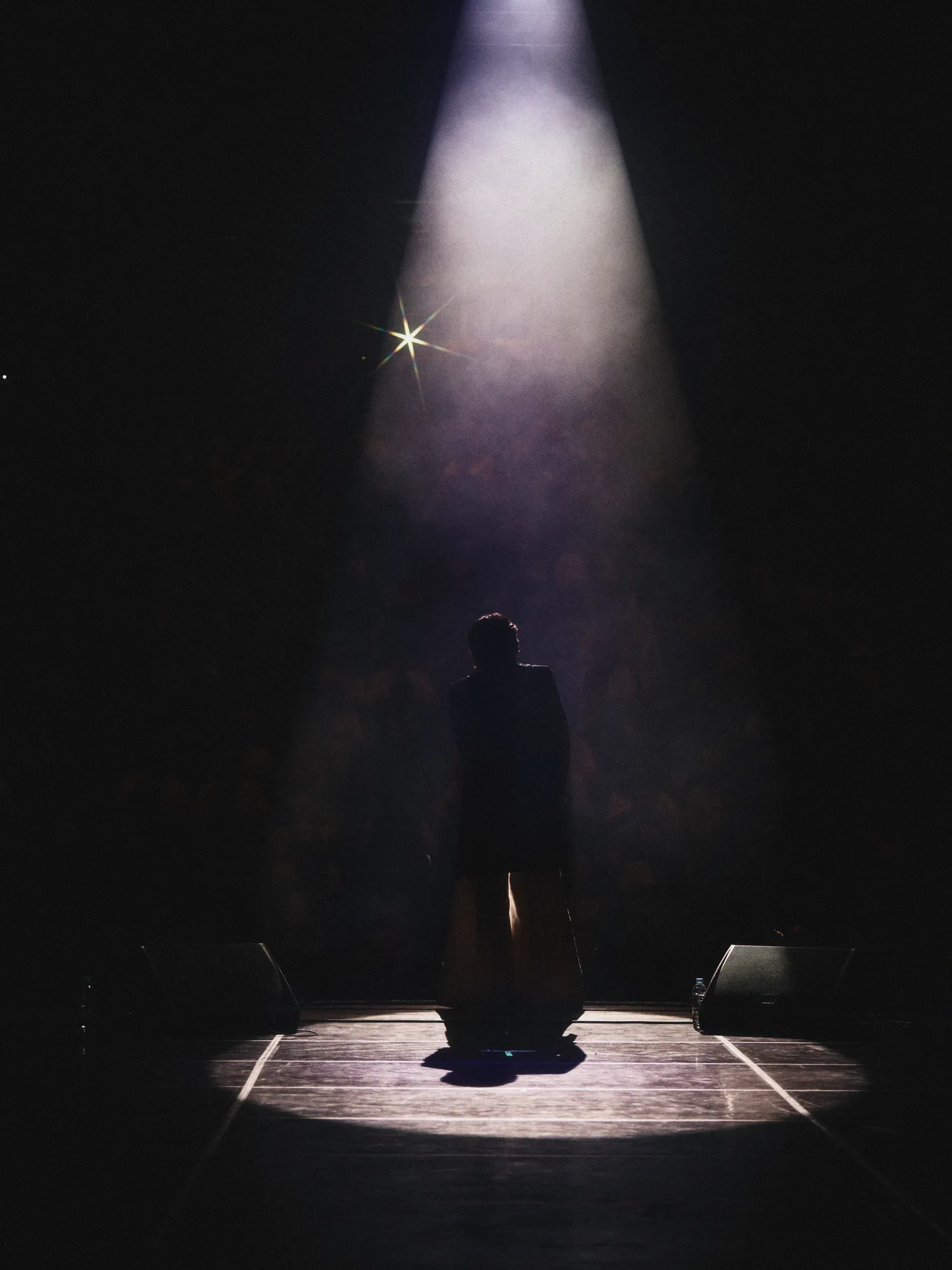 A black-and-white image of the performer singing under stage lights. Image 24.